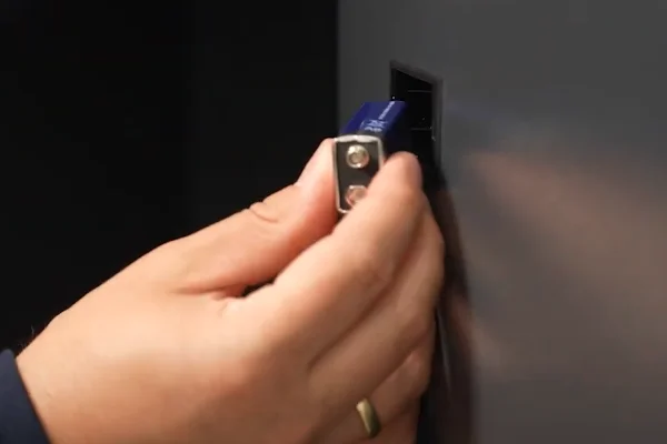 Hand schließt eine 9-Volt-Batterie am externen Batteriefach eines dunklen Tresors an – Notstromversorgung für das Elektronikschloss