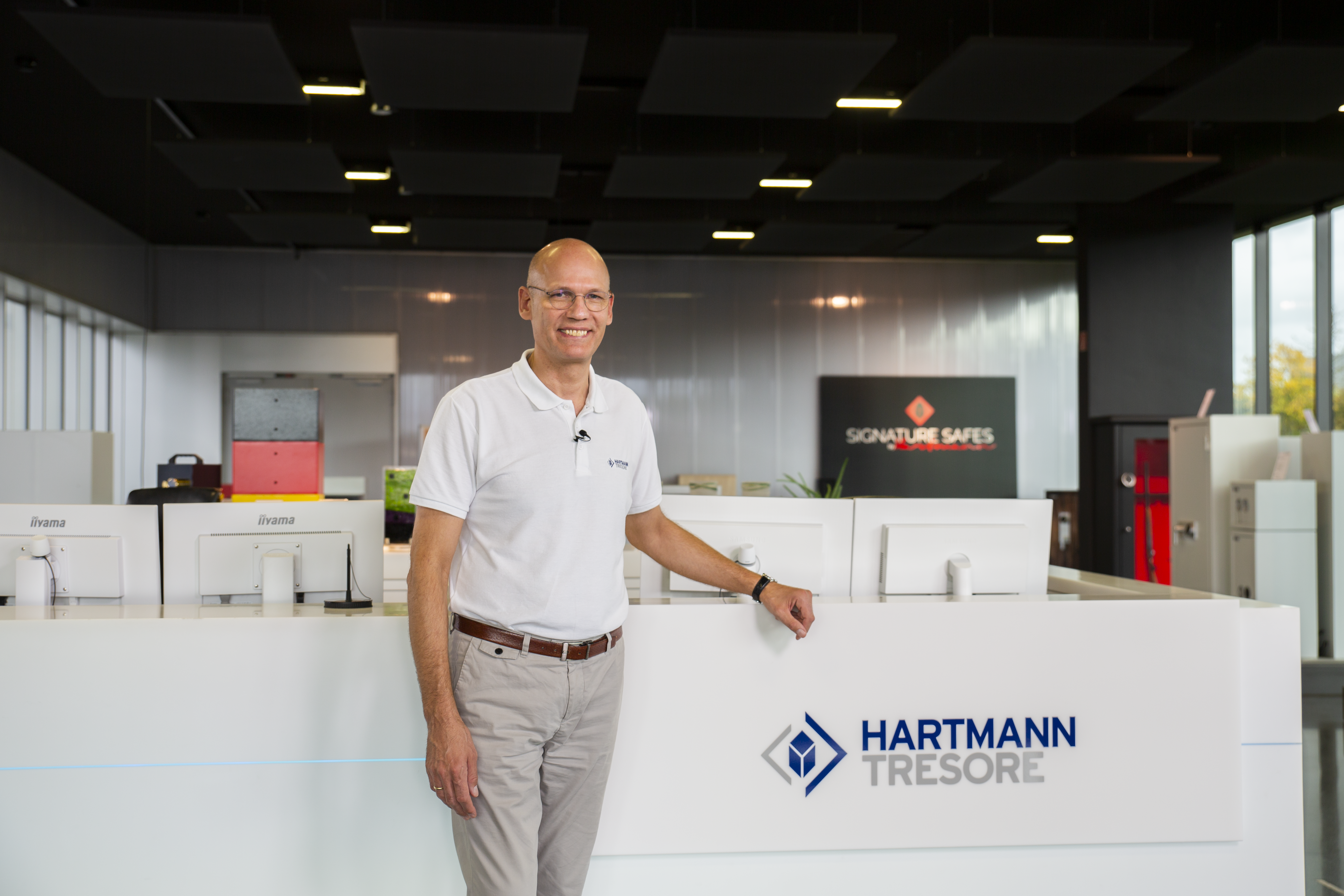 Geschäftsführer von HARTMANN TRESORE an der Empfangstheke mit Logo im Showroom, im Hintergrund Tresore und ein SIGNATURE SAFES Schild
