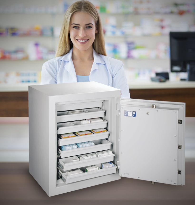 Apothekerin hinter einem geöffneten BTM-Tresor mit ausgezogenen Schubladen voller Medikamentenpackungen in der Apotheke