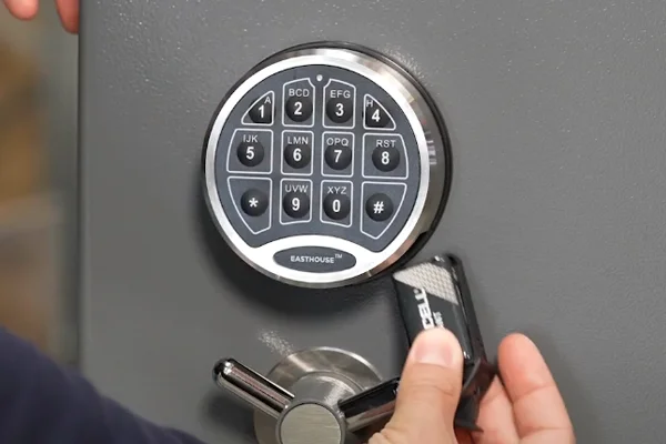 Hand hält eine Batterie zur Notstromversorgung an das elektronische Zahlenschloss eines EASTHOUSE-Tresors