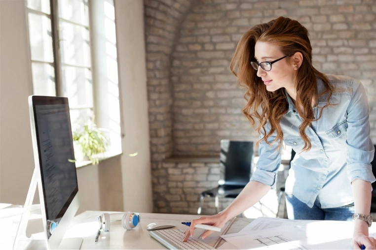 Eine Frau arbeitet stehend an ihrem Computer in ihrem Büro