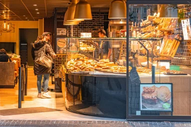 Blick von außen in eine Bäckereifiliale mit Brottheke und einer Kundin