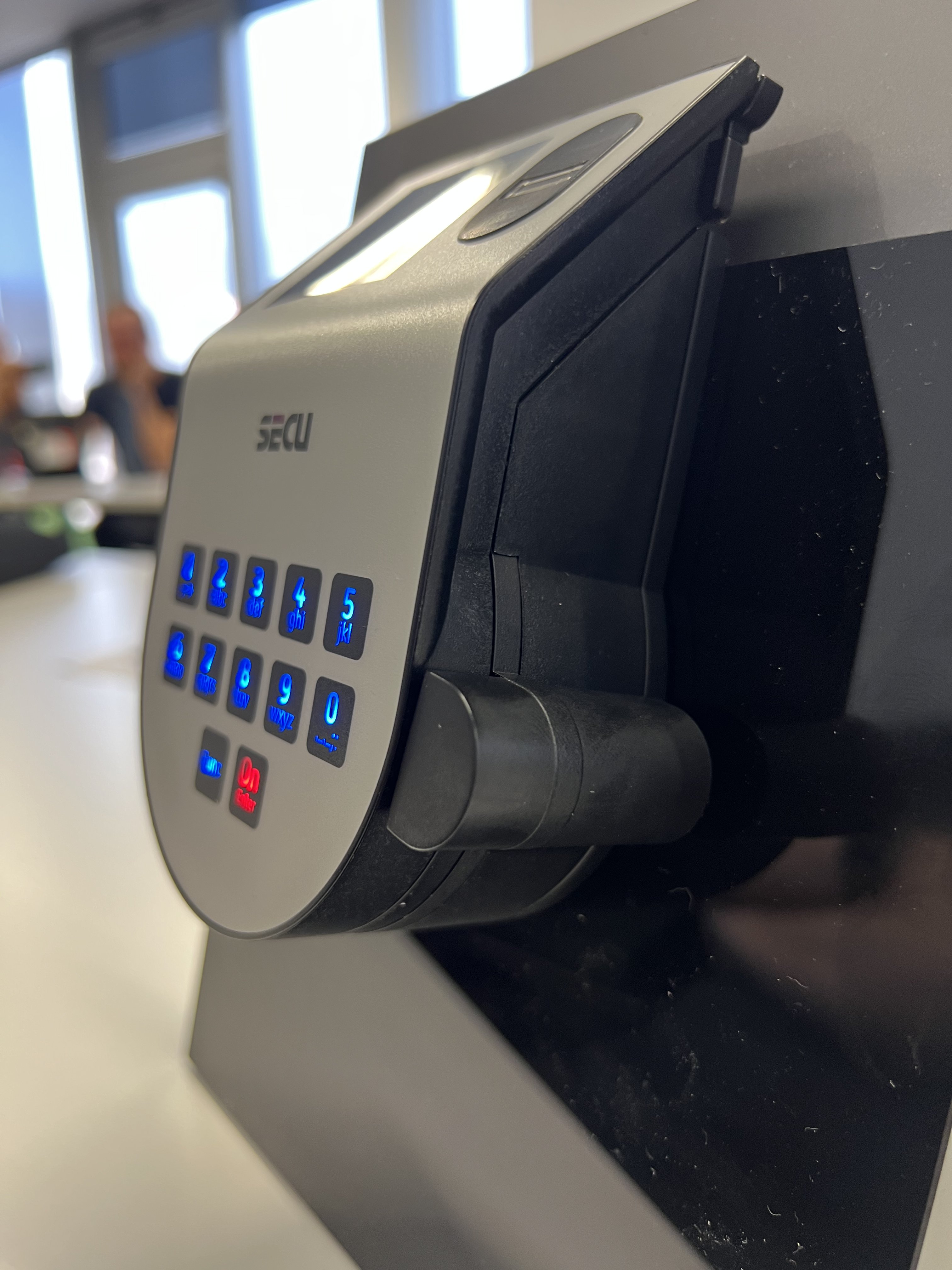 Seitenansicht eines SECU-Elektronikschlosses mit blau beleuchteter Tastatur und Drehknauf an einem Schulungsaufsteller