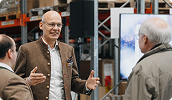 Berater im Gespräch mit Besuchern in einer Lagerhalle mit Hochregalen