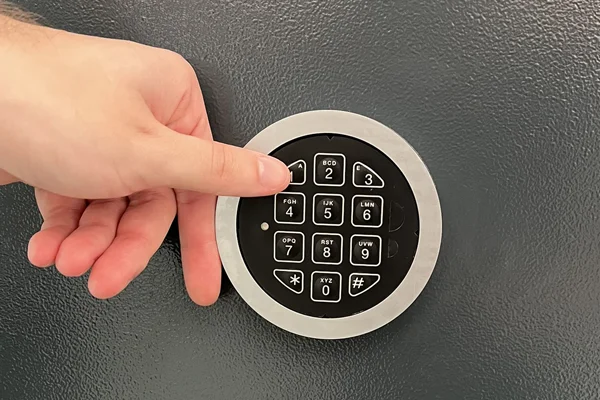 Hand tippt einen Code in das elektronische Zahlenschloss einer dunkelgrauen Tresortür