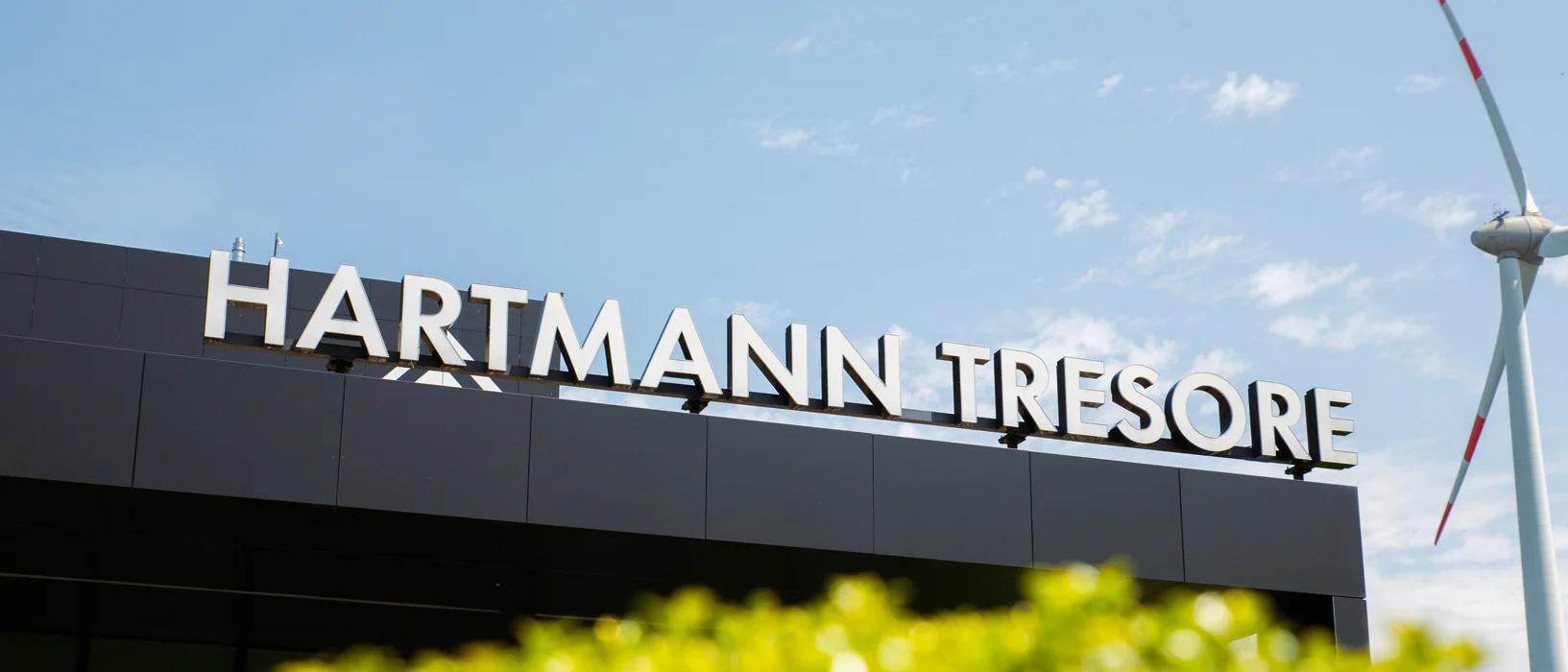 Schriftzug HARTMANN TRESORE auf dem Dach des Firmengebäudes in Paderborn, daneben ein Windrad