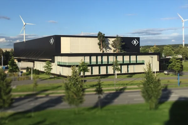 Firmengebäude von HARTMANN TRESORE in Deutschland mit dunkler Fassade und Rautenlogo, umgeben von Grünflächen und Windrädern