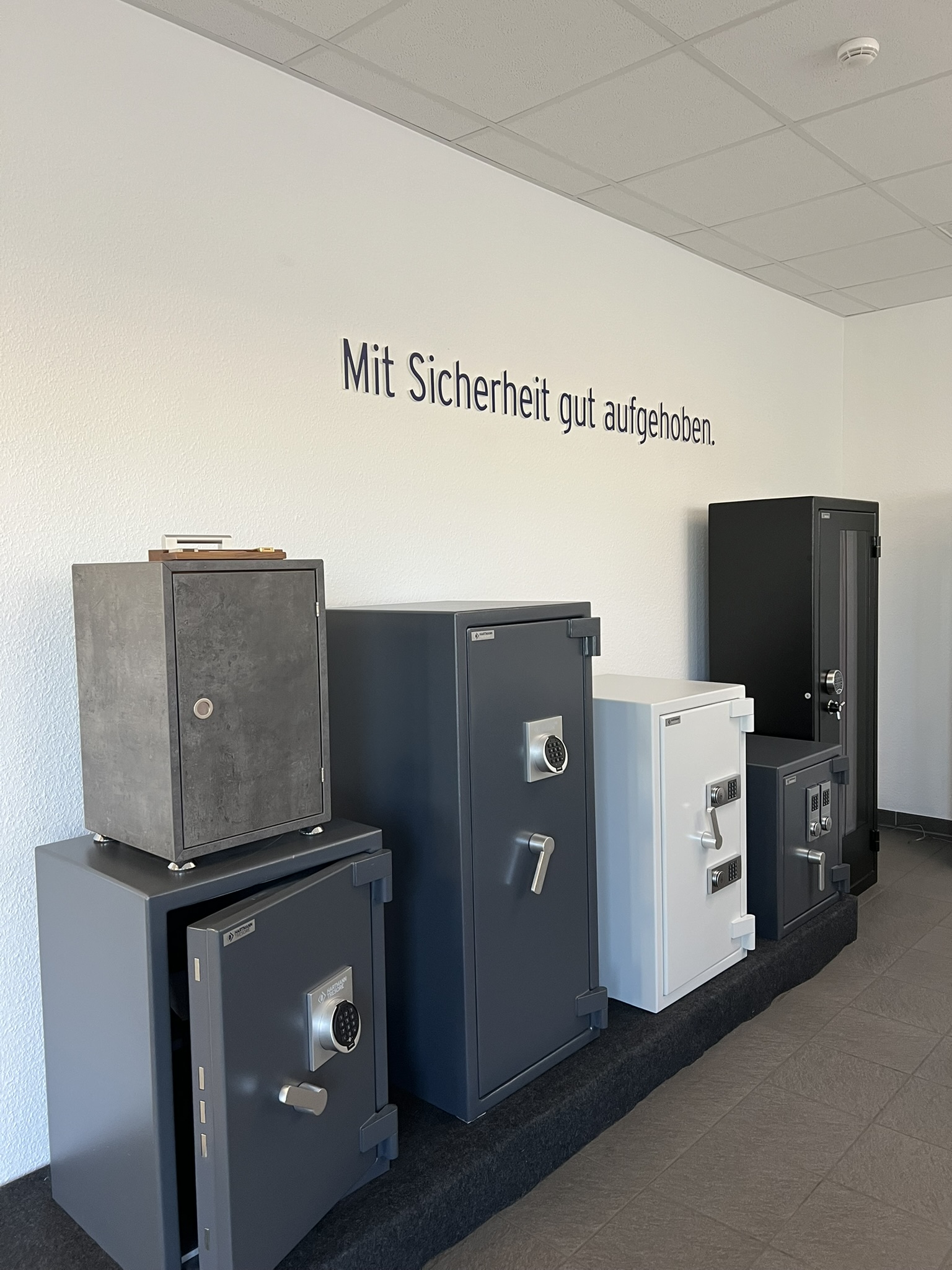 Showroom in Oberhausen mit sechs HARTMANN Tresoren in Grau, Weiß, Schwarz und Betonoptik unter dem Schriftzug „Mit Sicherheit gut aufgehoben.“