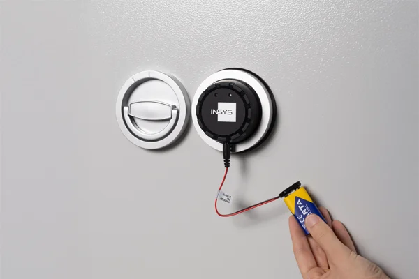 Elektronisches Tresorschloss von INSYS neben dem Klappgriff, mit externer 9-Volt-Batterie zur Notöffnung verbunden