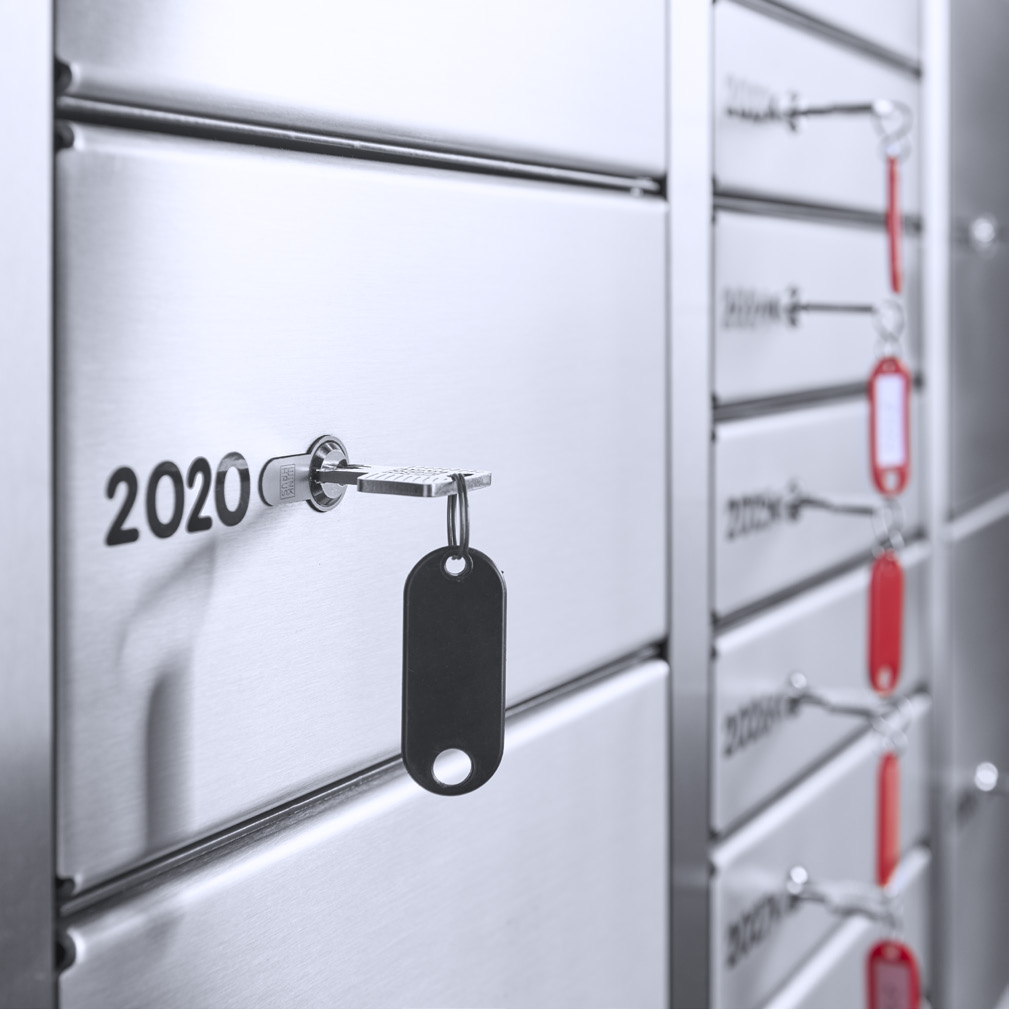 Schließfachanlage aus Edelstahl mit nummerierten Fächern und Schlüsselschlössern. Im Vordergrund steckt ein Schlüssel im Fach „2020“ mit schwarzem Schlüsselanhänger. Ideal für Banken, Hotels oder sichere Aufbewahrung in Unternehmen.